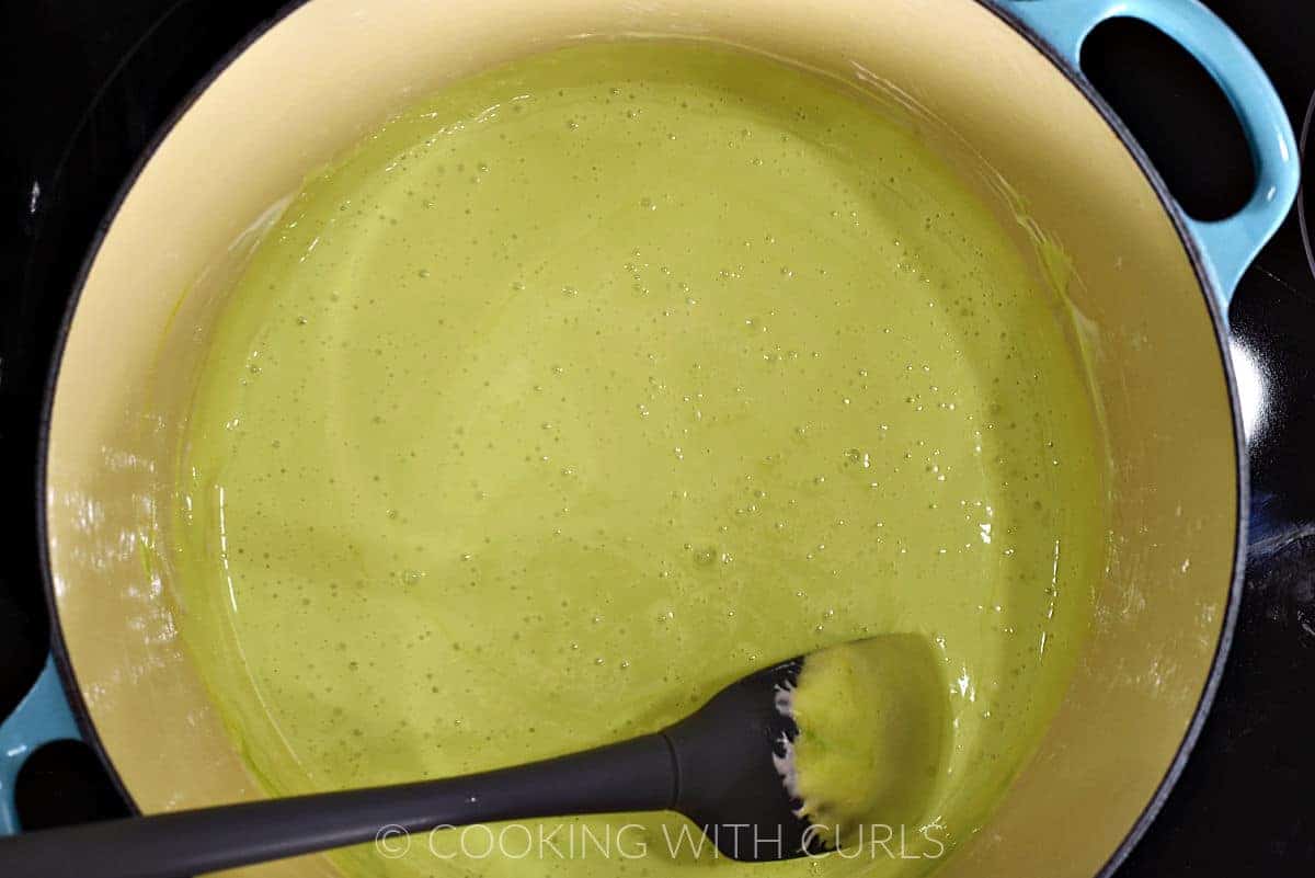 Green colored melted marshmallows in a large pot with a silicone spatula on the side. 