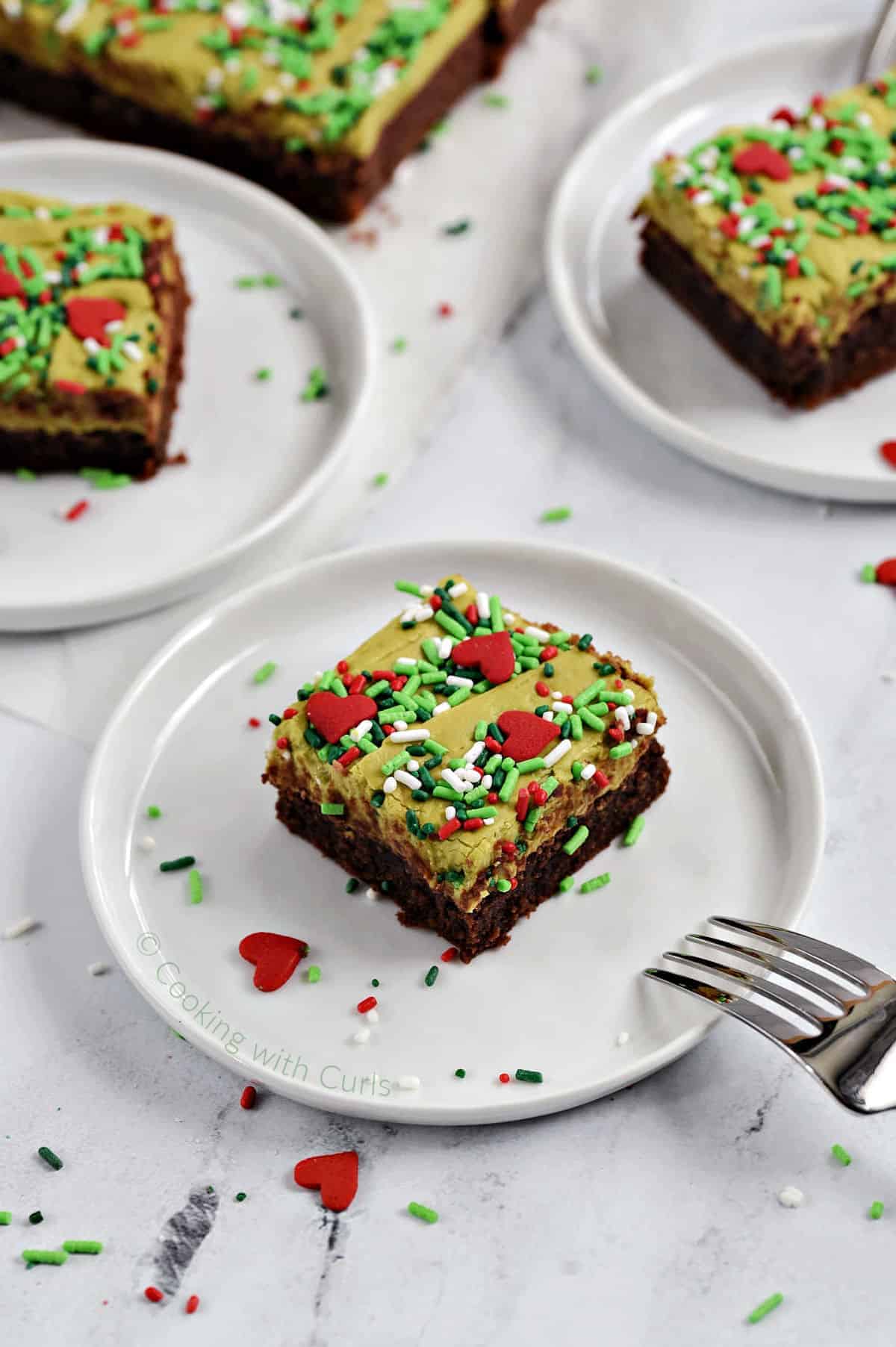 Green fudge topped brownies with sprinkles on small white plates.