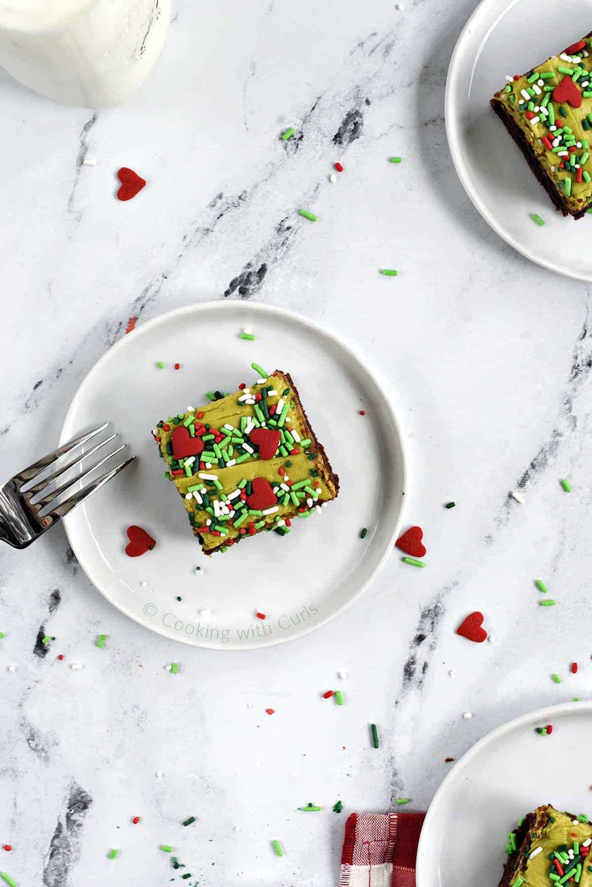Three grinch brownies on small plates with a glass of milk in the background.