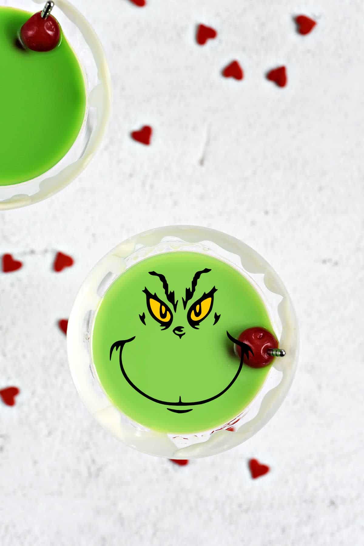 Looking down on a green Grinch Martini with white drizzle around the rim of the martini glass and a Grinch face in the center.