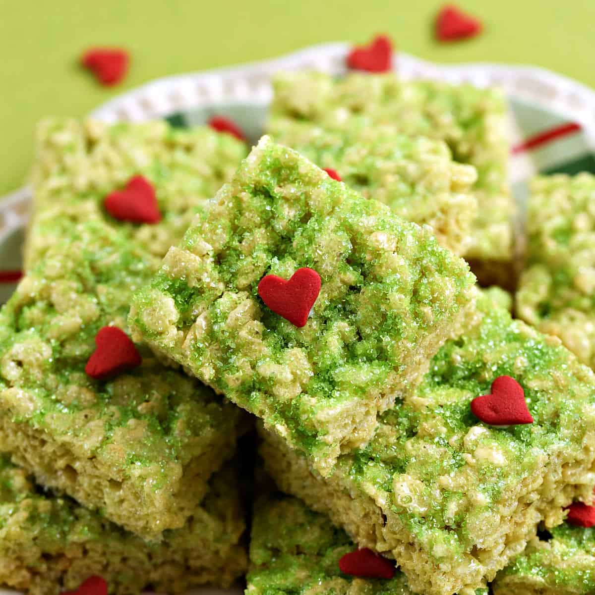 A pile of green rice krispie treats with red hearts piled on a plate .