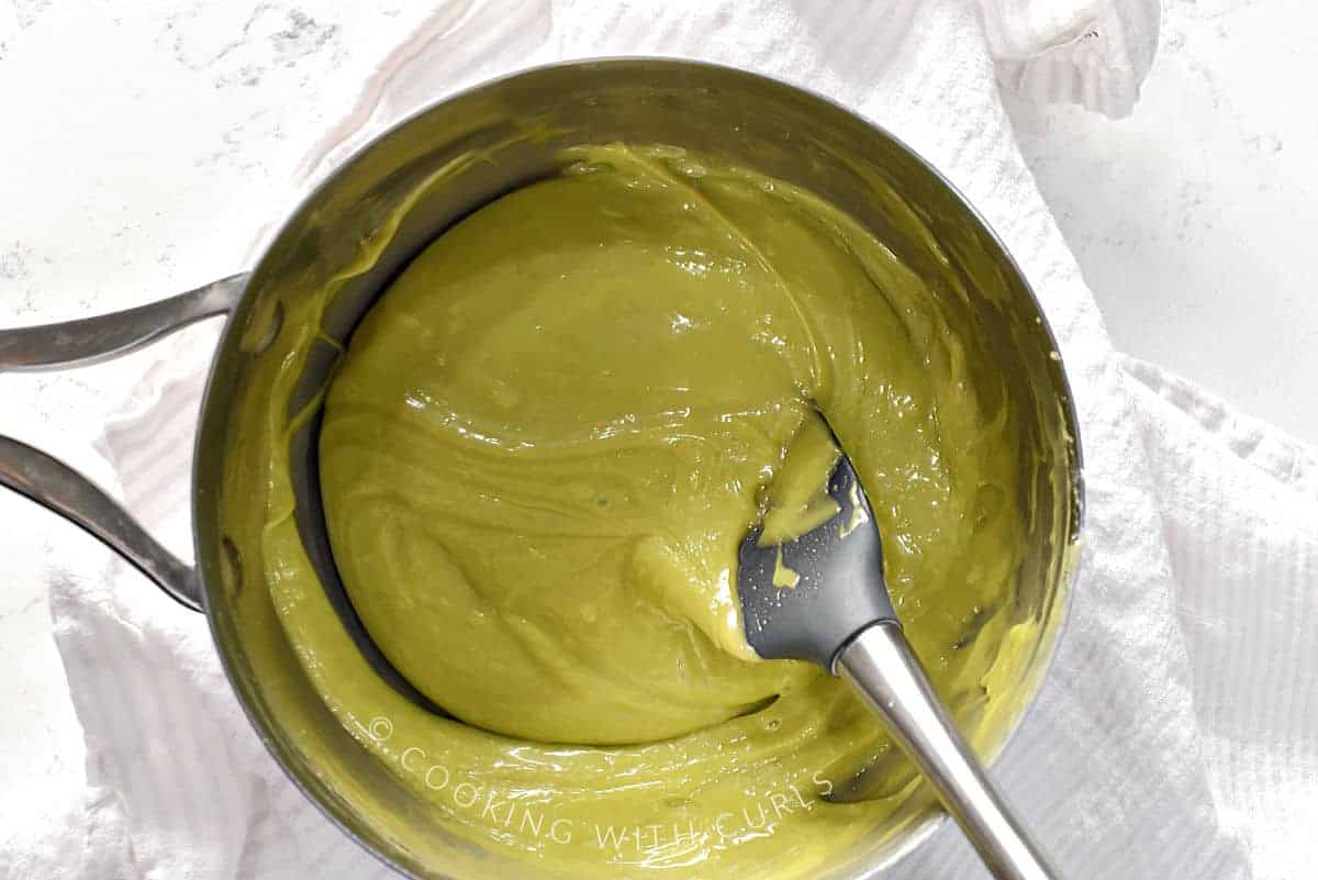 Grinch green fudge in a saucepan with a silicone spatula on the side. 