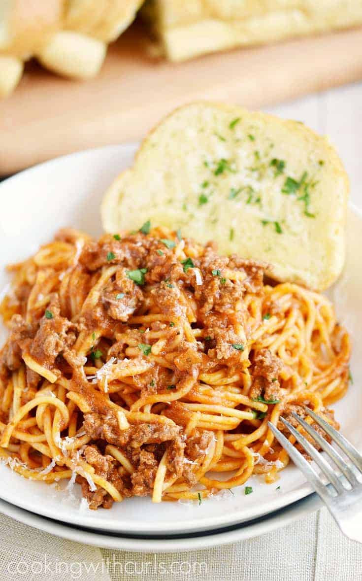 A plate of spaghetti covered in meat sauce with garlic bread on the side.