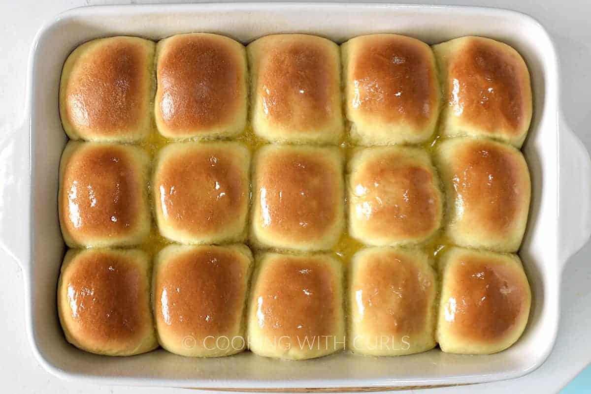 Melted butter brushed over 15 baked dinner rolls in a white baking pan. 