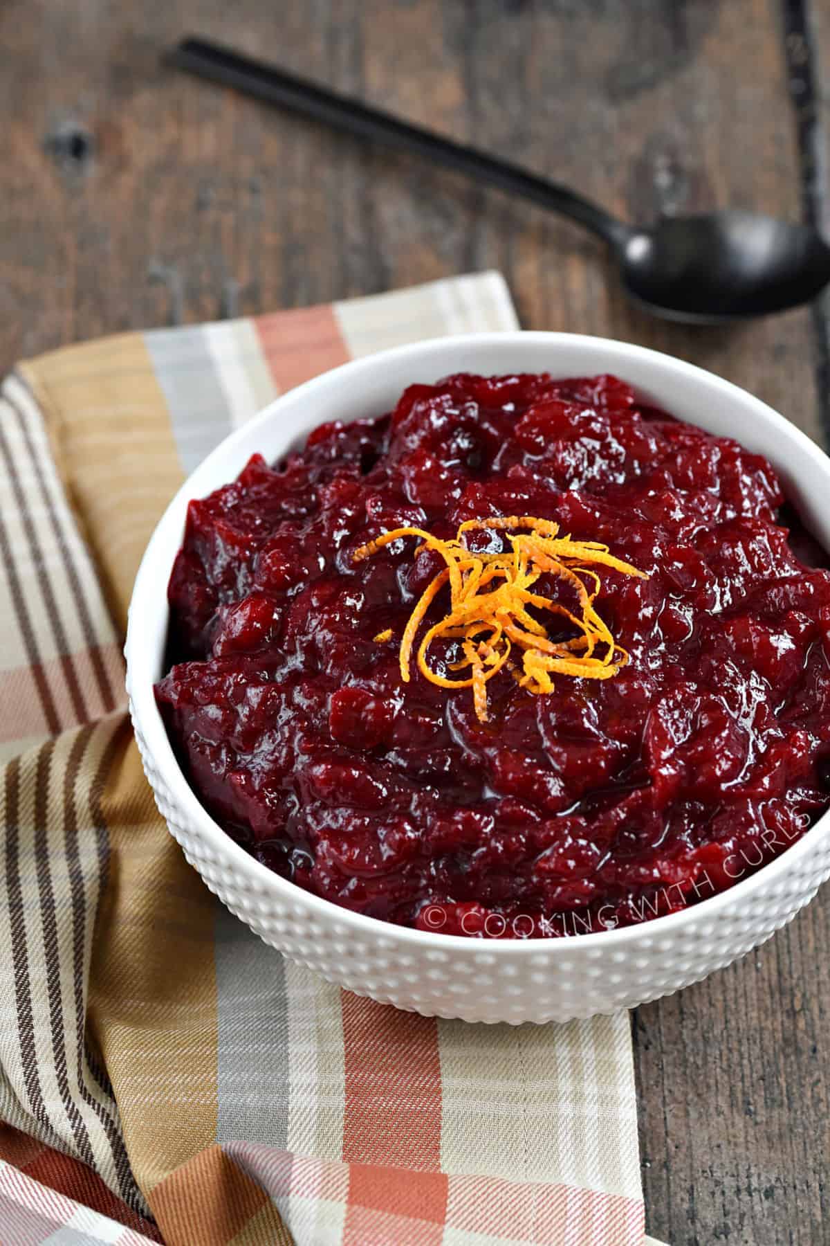 Orange Amaretto Cranberry Sauce garnished with strips of orange zest in a serving bowl with a black spoon in the background.