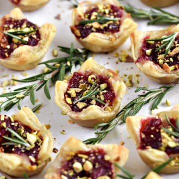 Puff Pastry Cranberry Brie Bites topped with fresh rosemary and chopped pistachios.