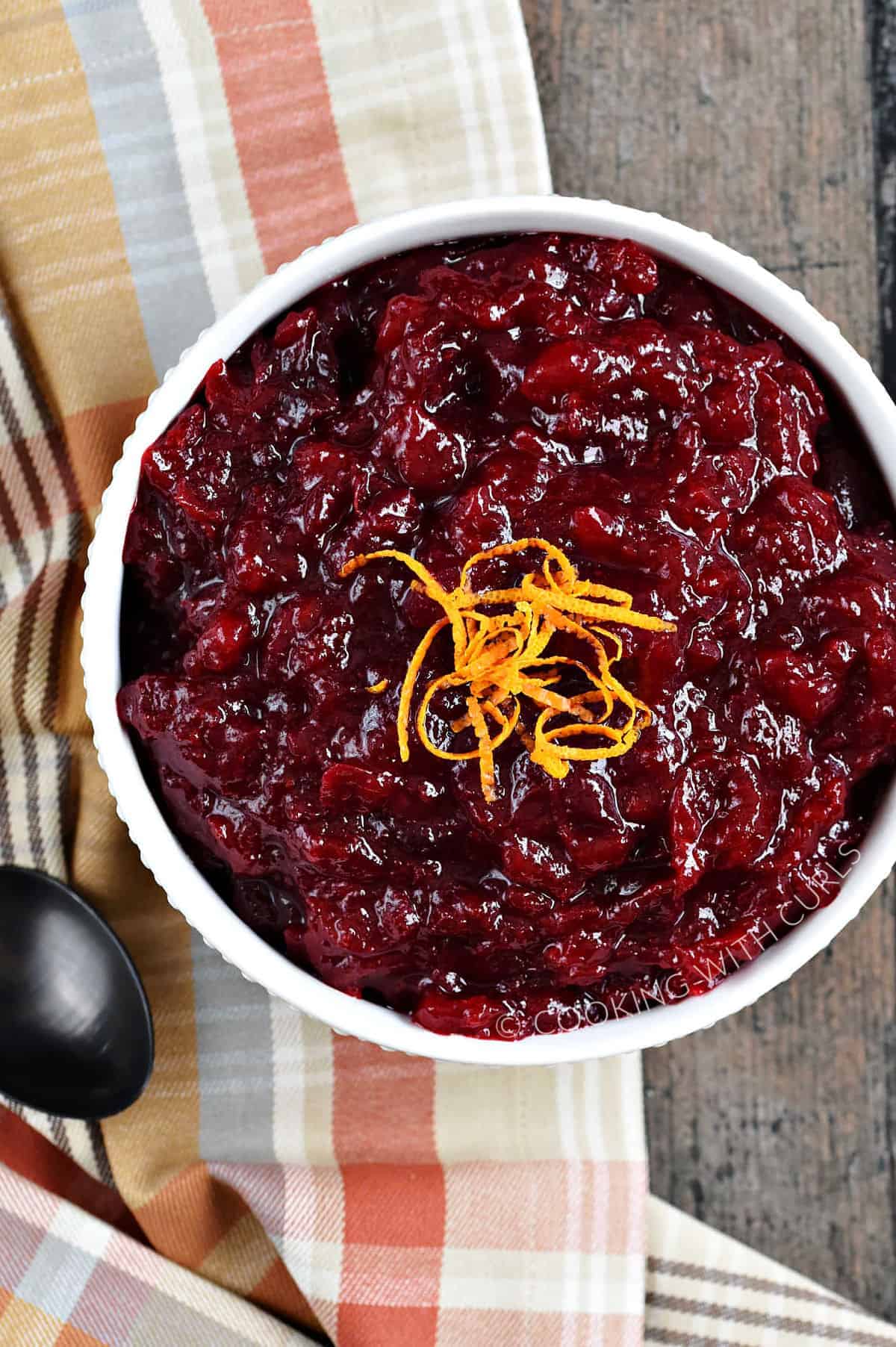 Looking down on a bowl of tart Orange Amaretto Cranberry Sauce sitting on a plaid, fall-colored napkin.