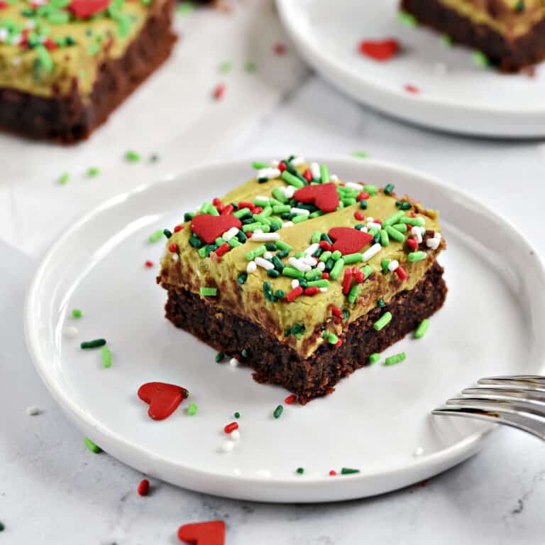 Green fudge topped brownies with sprinkles on small white plates.