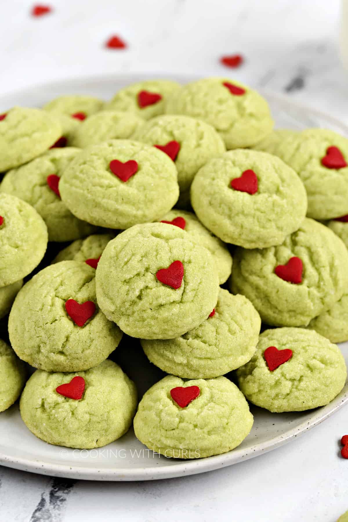 A plate filled with crinkly green sugar cookies with a small red heart in the center.