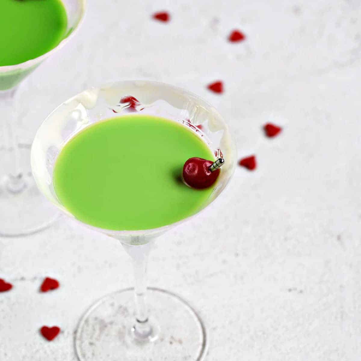 A green Grinch Martini with a cherry surrounded by tiny red hearts.