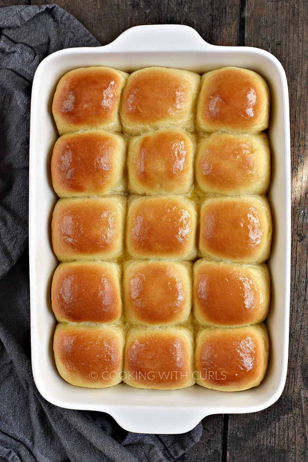 Looking down on 15 butter-topped dinner rolls in a white baking pan.