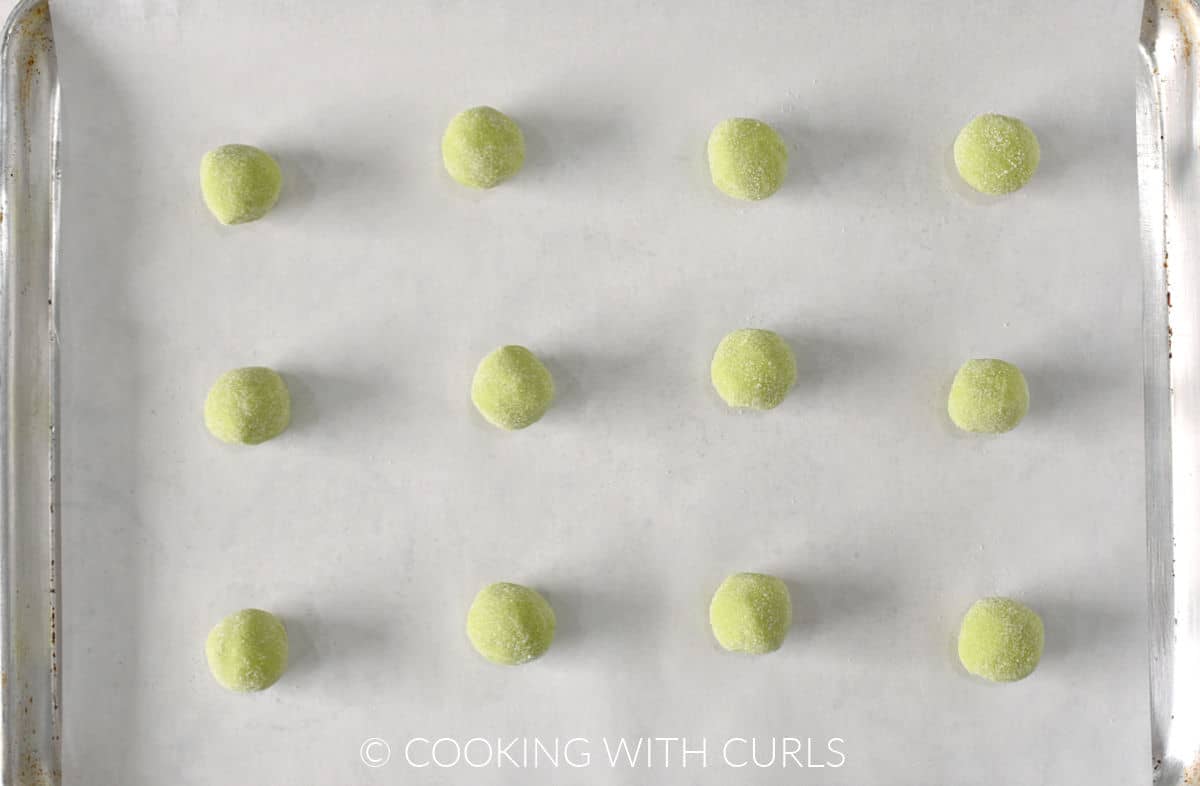 Twelve sugar coated green cookie balls on a parchment lined baking sheet. 