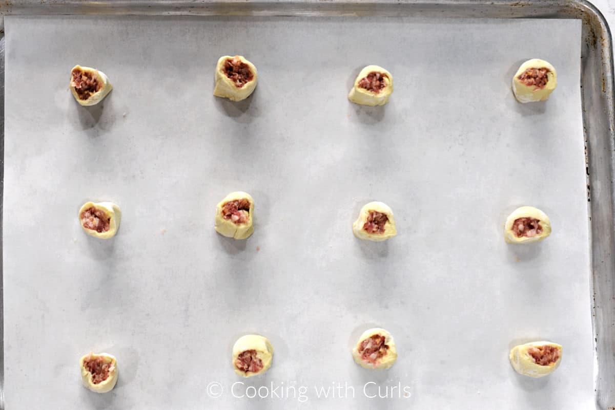 Twelve unbaked puff pastry sausage bites on a parchment lined baking sheet. 