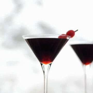 Two cherry cheesecake martinis with cherry garnish in front of a white background.