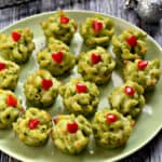Fifteen Grinch green Mac and Cheese Bites with red hearts on a green plate.