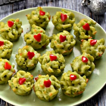 Fifteen Grinch green Mac and Cheese Bites with red hearts on a green plate.