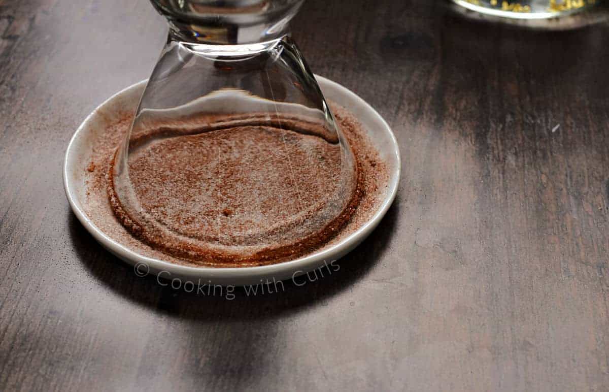 The rim of a martini glass in a plate filled with cinnamon sugar. 