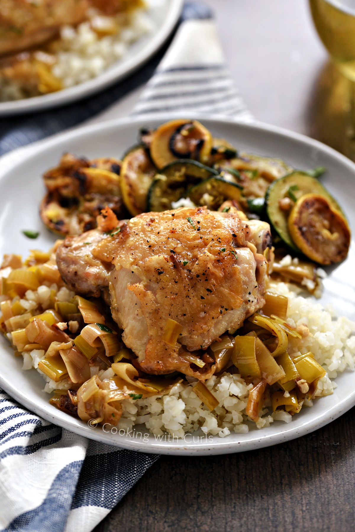 A chicken thigh on a bed of rice and leeks with sautéed zucchini and squash on the side. 