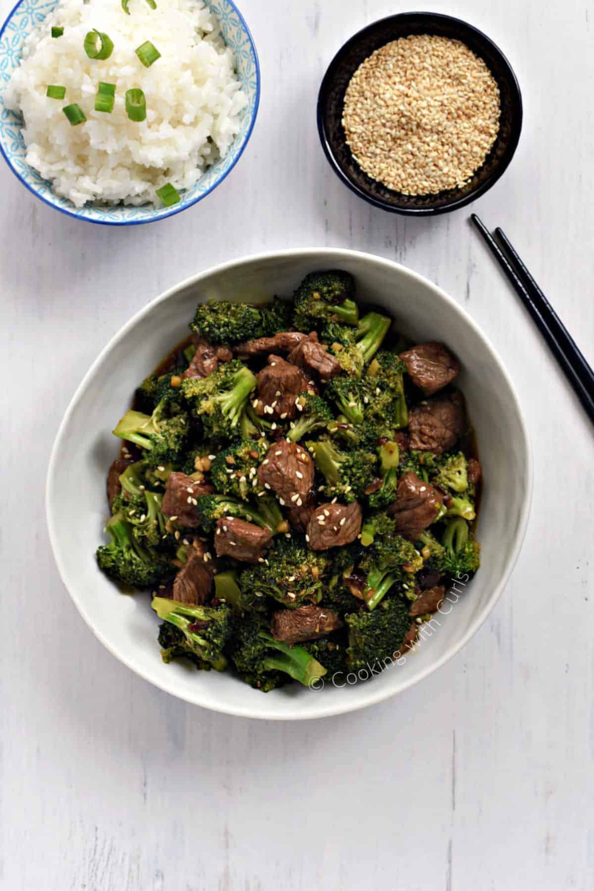 Strips of beef and broccoli florets coated in sauce and sprinkled with sesame seeds in a large bowl.