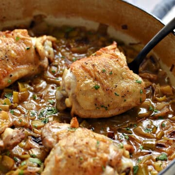 Three chicken thighs cooked with leeks in a skillet.
