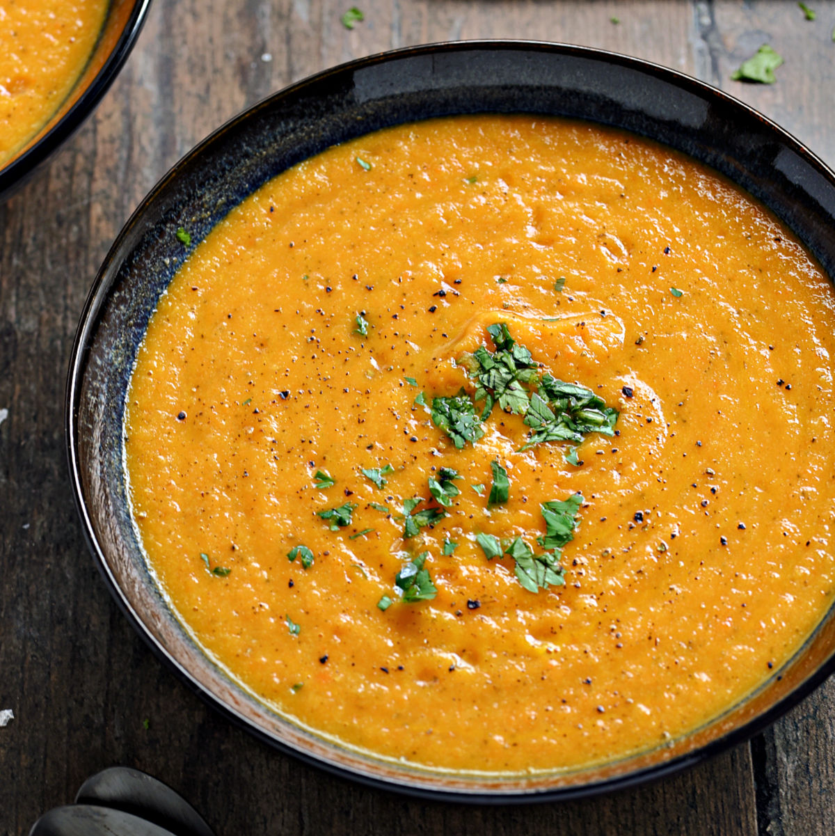 A bowl of creamy carrot and cauliflower soup topped with chopped parsley and black pepper.
