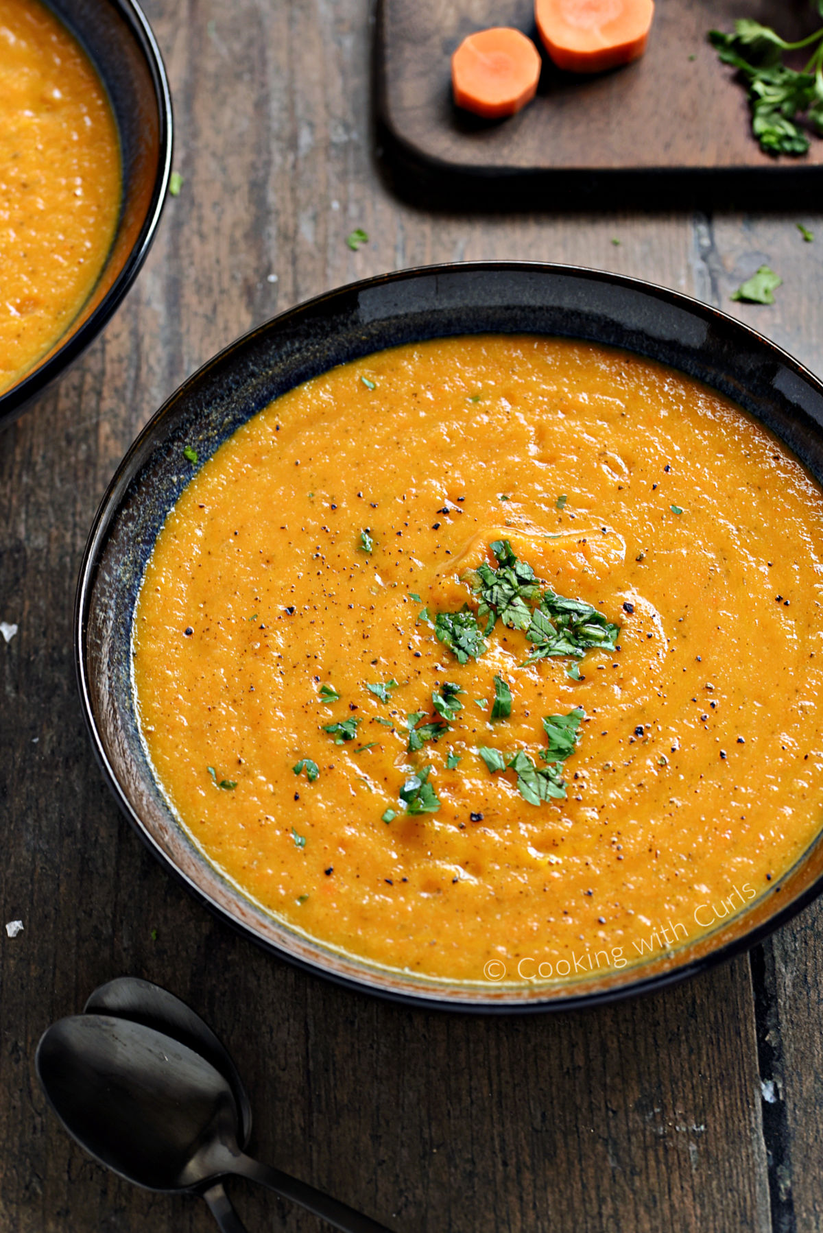 Creamy Carrot and Cauliflower Soup in a large bowl with chopped parsley and black pepper.