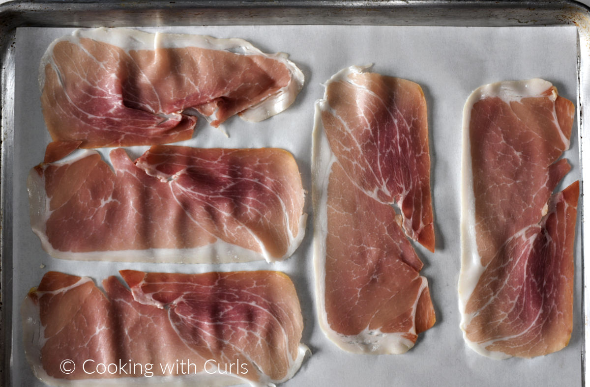Five slices of prosciutto on a parchment paper lined baking sheet. 