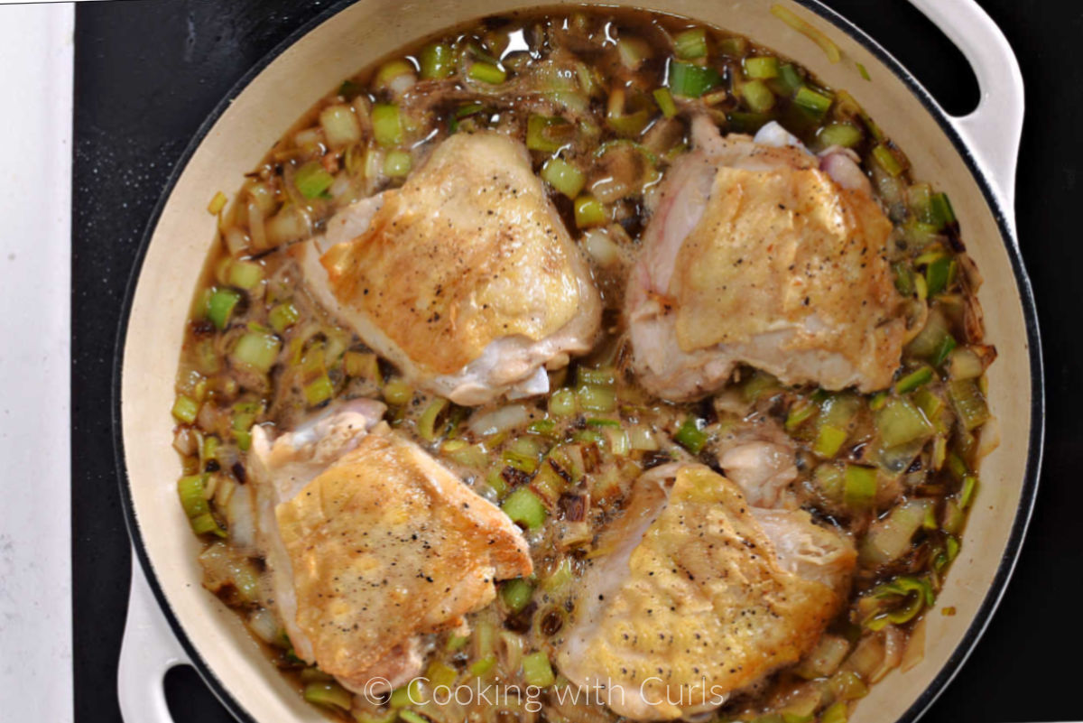 Four chicken thighs in a skillet with sautéed leeks. 