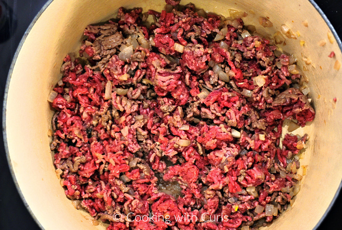 Ground beef mixed with diced onions in a large pot. 