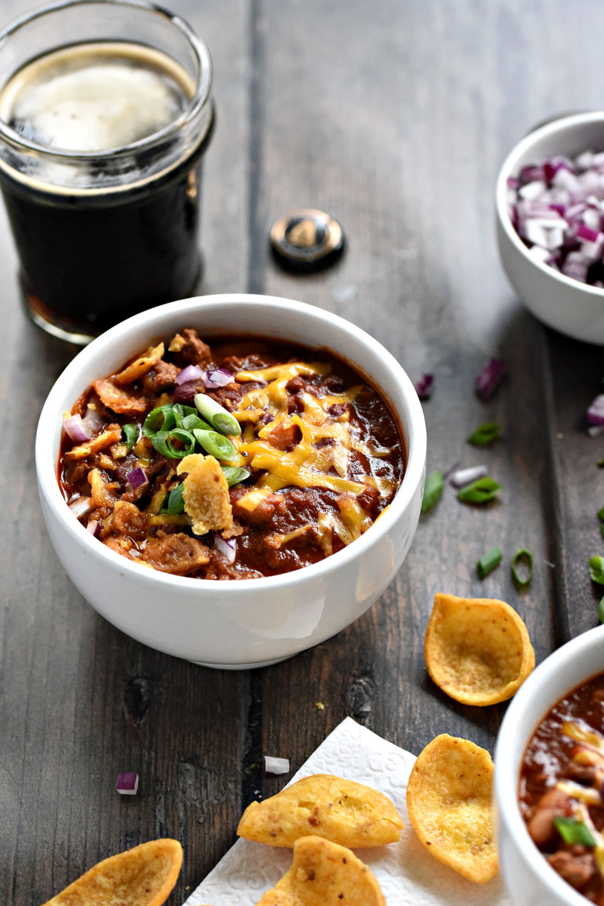A bowl of Guinness Stout Chili with Beef and beans topped with cheddar cheese, sliced green onions and crushed corn chips. 
