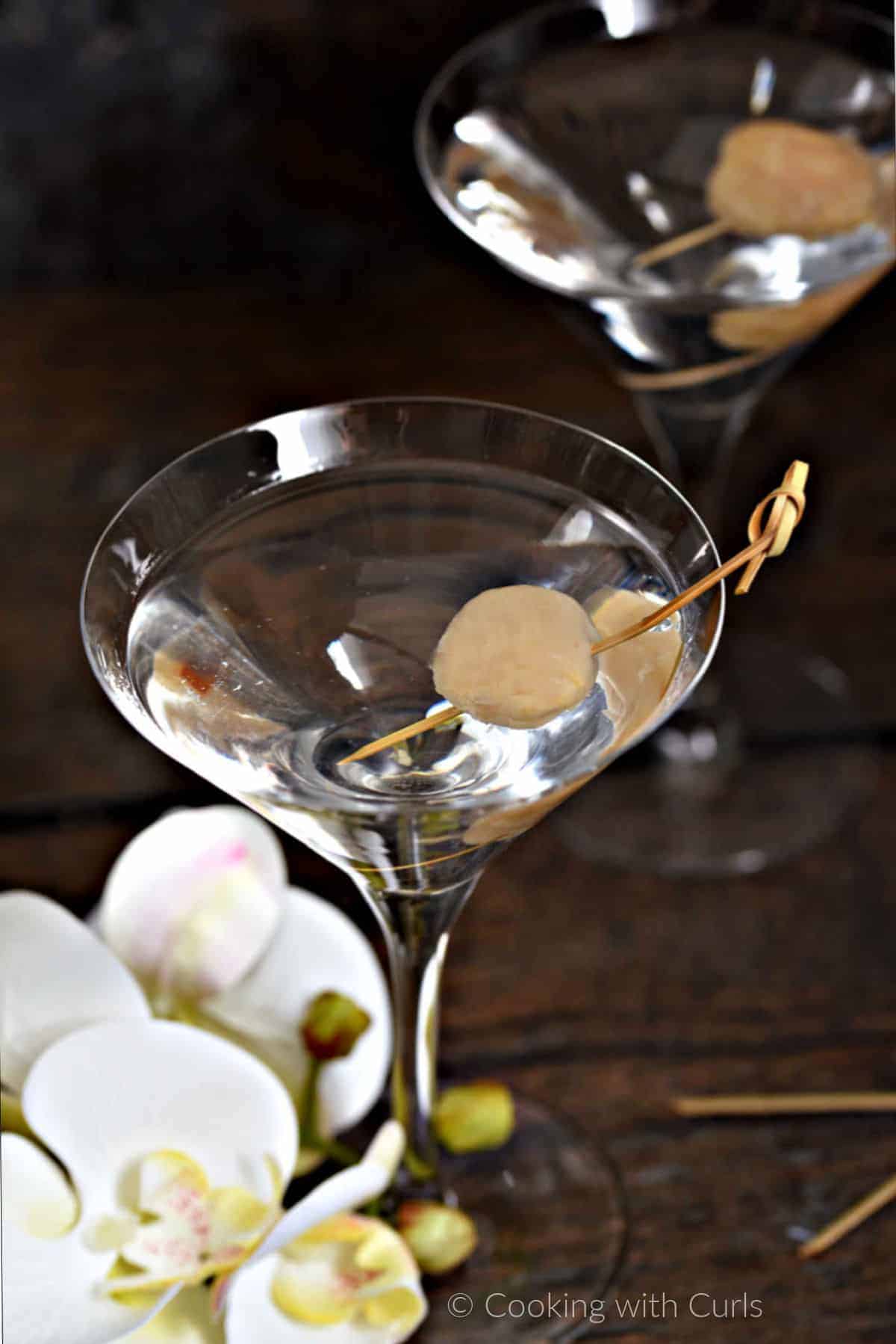 Two lychee martinis in martini glasses garnished with a lychee skewered with a bamboo cocktail stick.