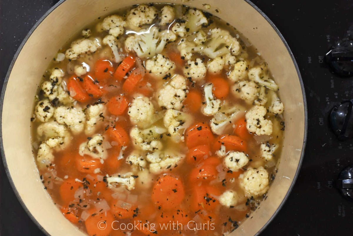 Sliced carrots and chopped cauliflower in a large pot with chicken stock, onions, and seasonings. 