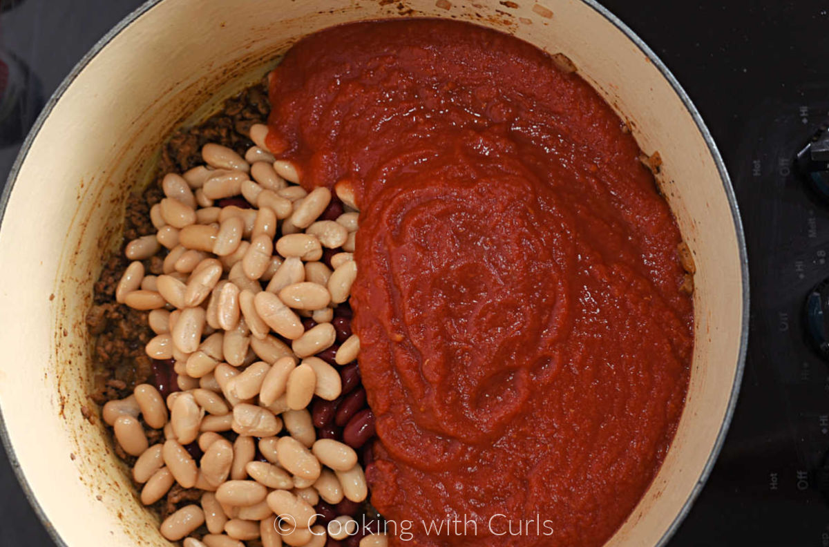 White and red kidney beans with crushed tomatoes on top of the beef mixture in a large pot. 