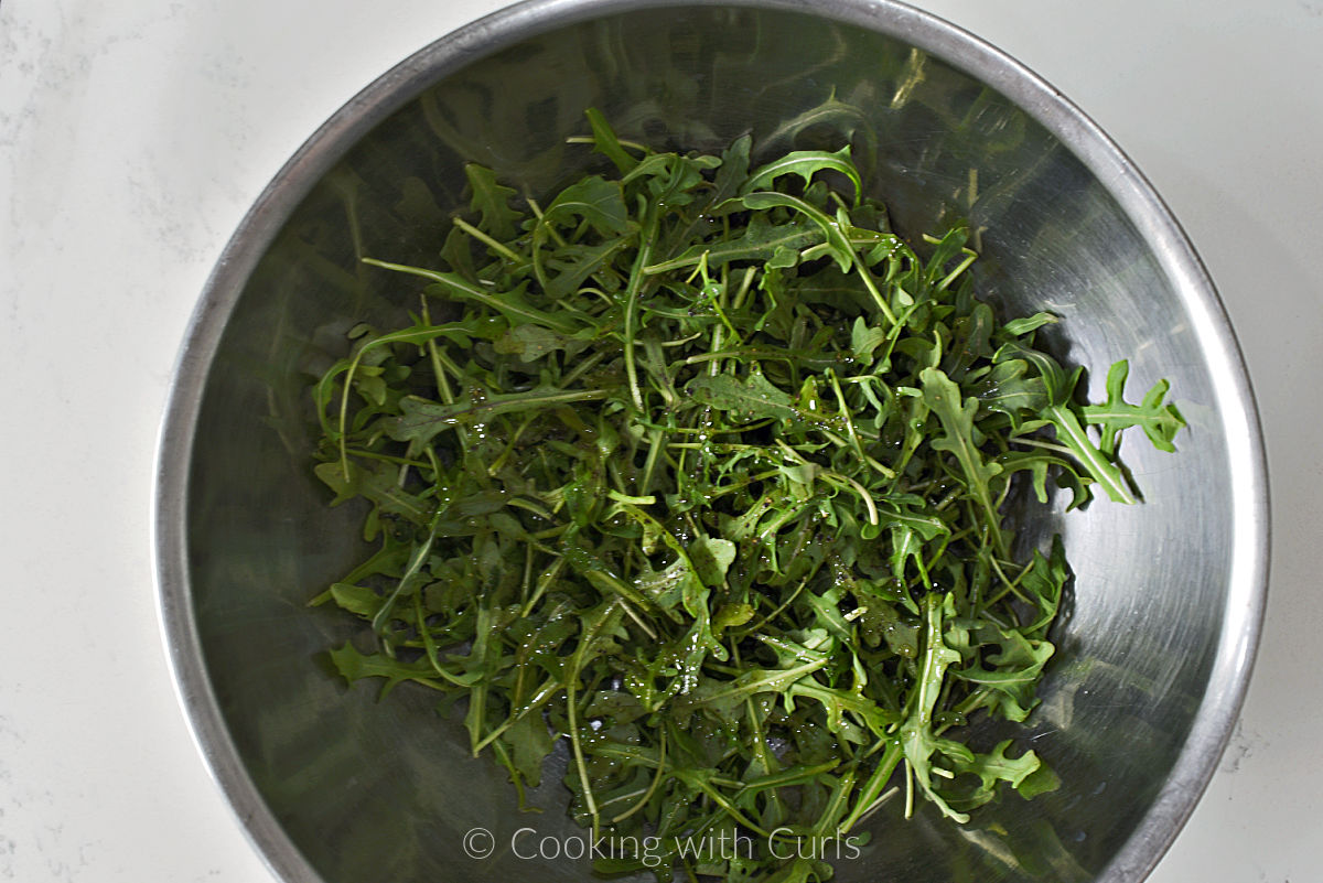 Arugula leaves tossed with oil and pepper in a large bowl. 