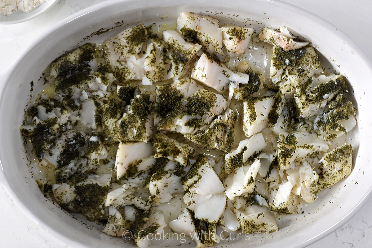 Baked cod with wine and dill flaked apart in a baking dish.