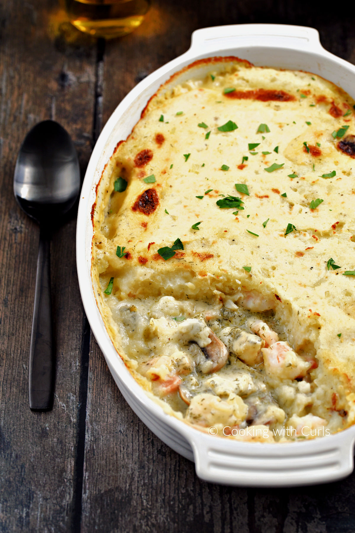 Mashed potato topped fish pie in an oval baking dish with the front quarter of the ingredients removed.