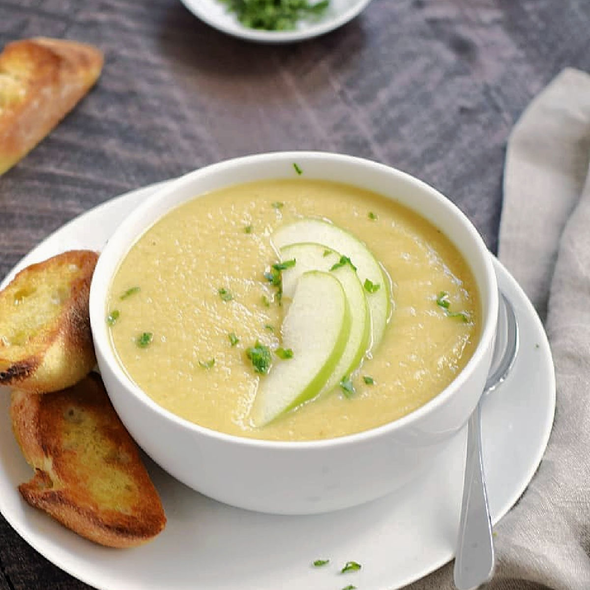 A bowl of creamy parsnip and apple soup topped with green apple slices.