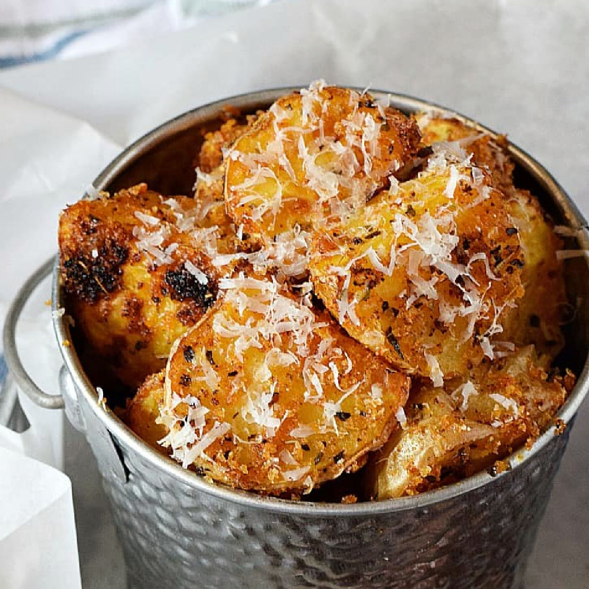 Crispy roast potato cubes in a metal bucket topped with parmesan cheese and Italian seasoning.