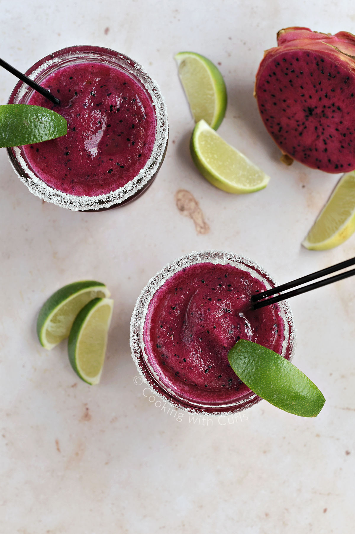 Looking down on two dragon fruit margaritas surrounded by lime wedges and a fresh dragon fruit.