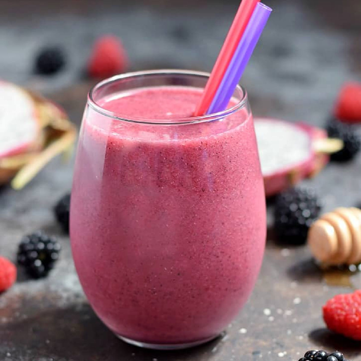 Bright pink dragon fruit smoothie in a small glass surrounded by fresh berries.