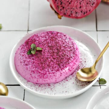 Pink panna cotta on a small plate sprinkled with dragon fruit powder.