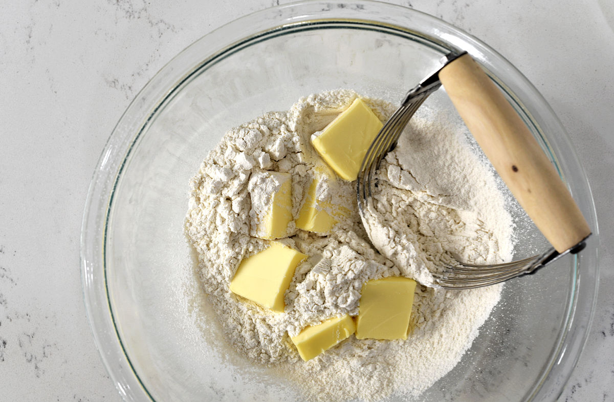 Flour mixture and butter cubes in a large bowl with pastry cutter. 