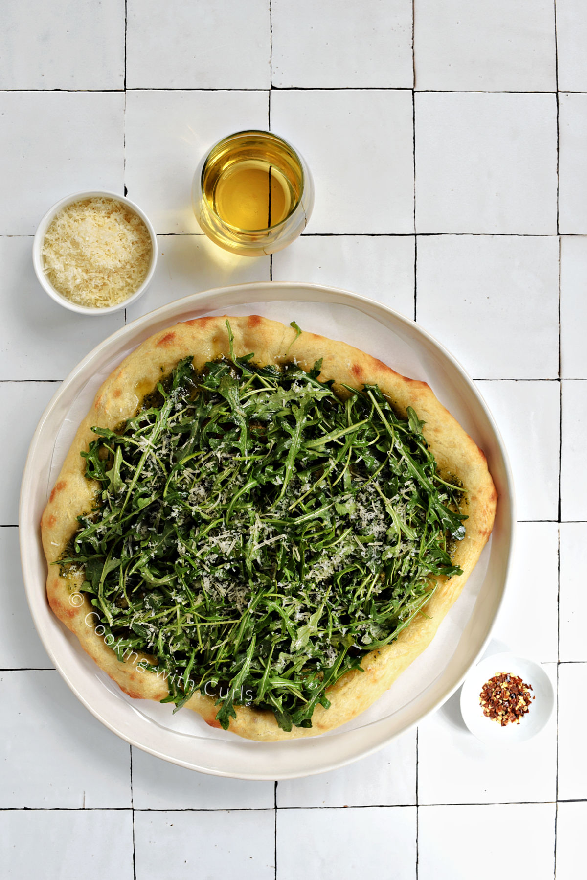 Looking down on a greens pizza topped with arugula, basil pesto, and grated parmesan cheese.