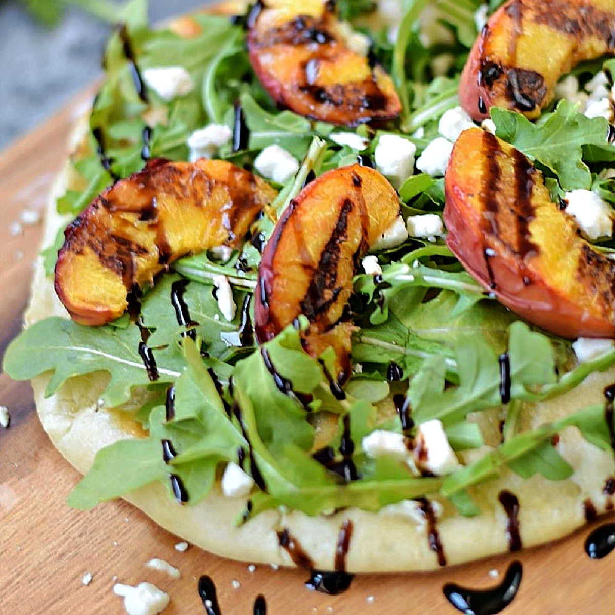 Pizza crust topped with arugula, grilled peaches, crumbled cheese and drizzled with balsamic glaze.