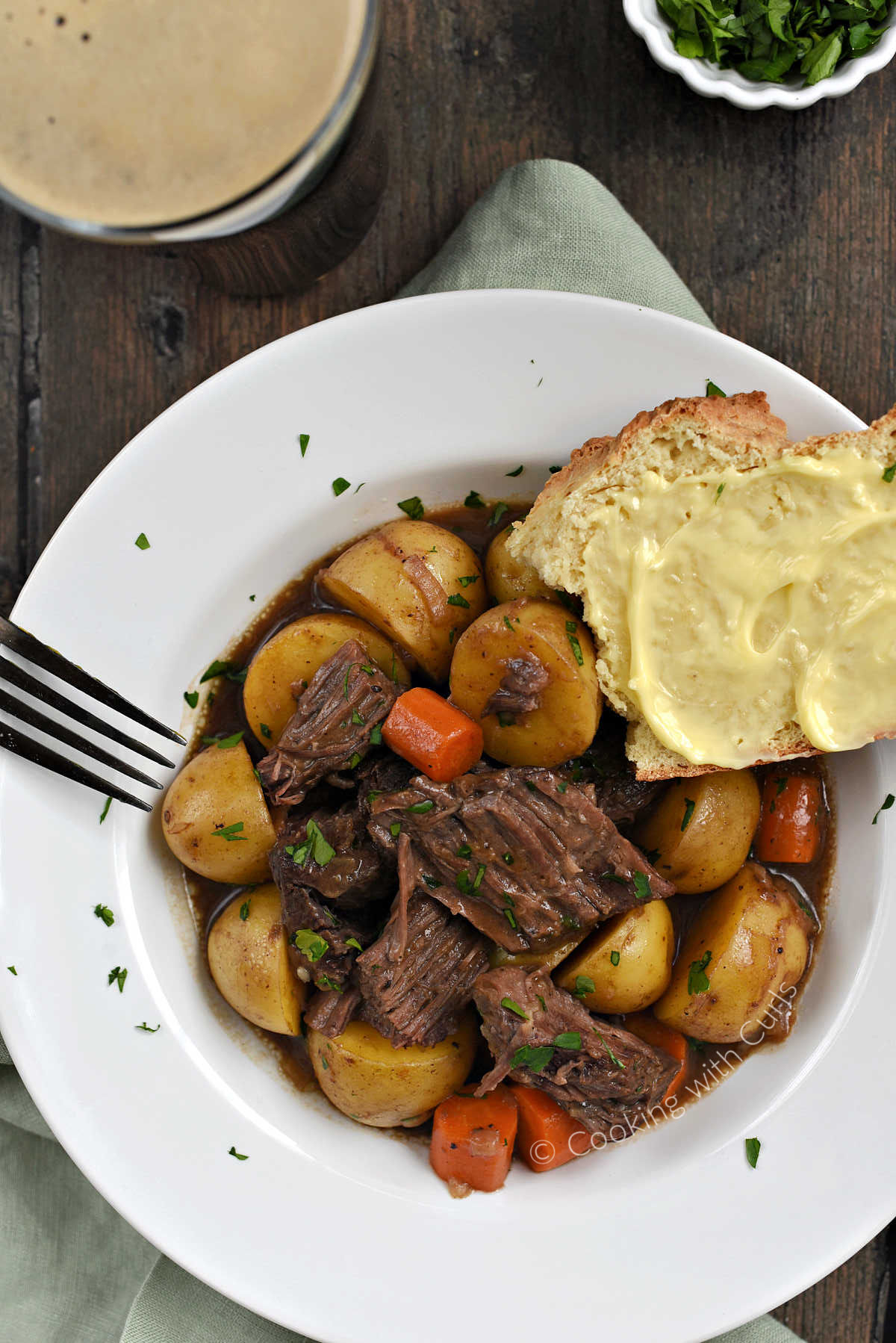 Looking down onGuinness Beer Pot Roast with carrots, potatoes, and gravy in a bowl with a slice of buttered bread resting on the rim.