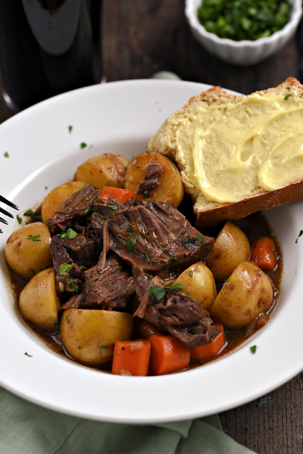 Chunks of beef roast, potatoes, and carrot slices in a Guinness stout gravy with buttered bread on the edge of the bowl.