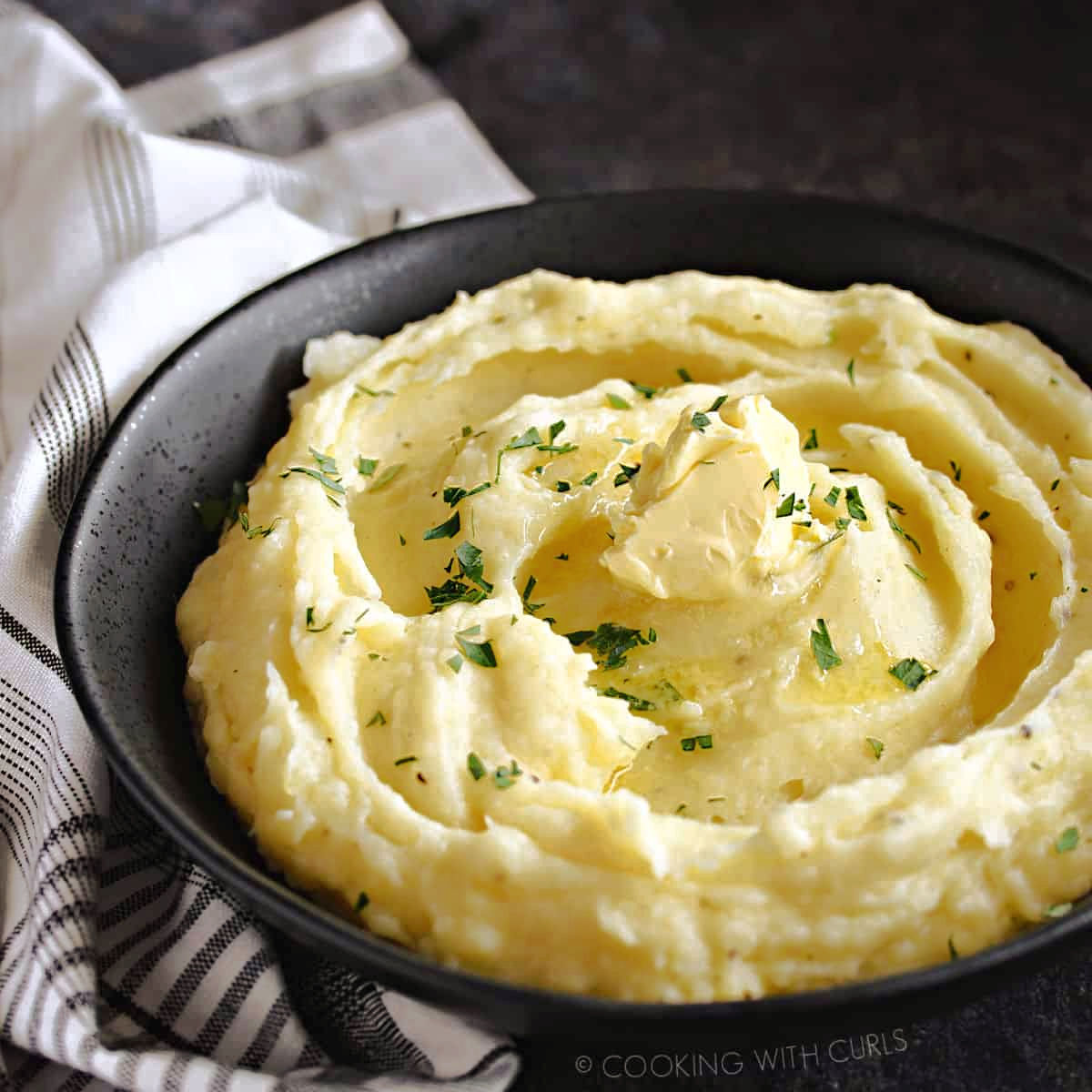 A bowl of creamy mashed potatoes topped with butter and parsley.