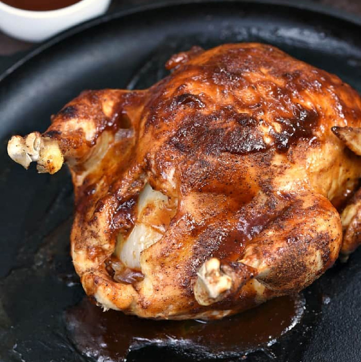 Whole chicken covered in barbecue sauce on a cast iron skillet.