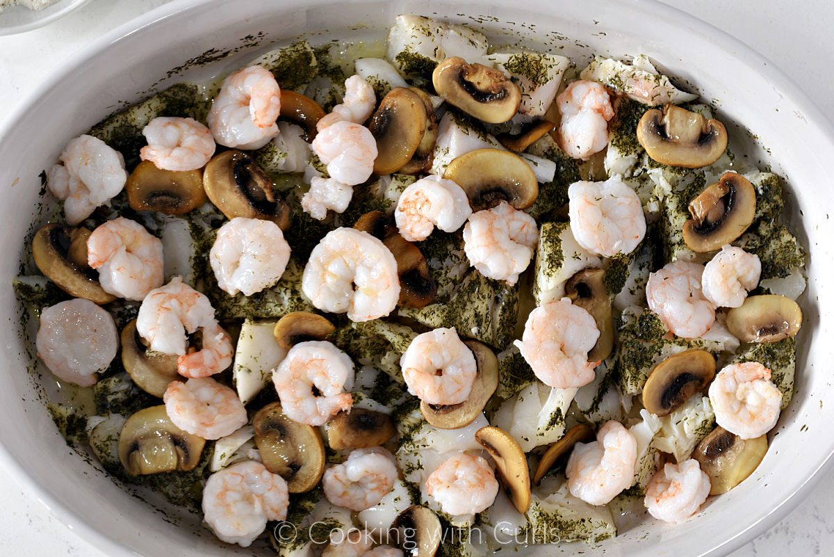 Mushrooms and shrimp on top of  baked cod, wine, and dill in a baking dish. 