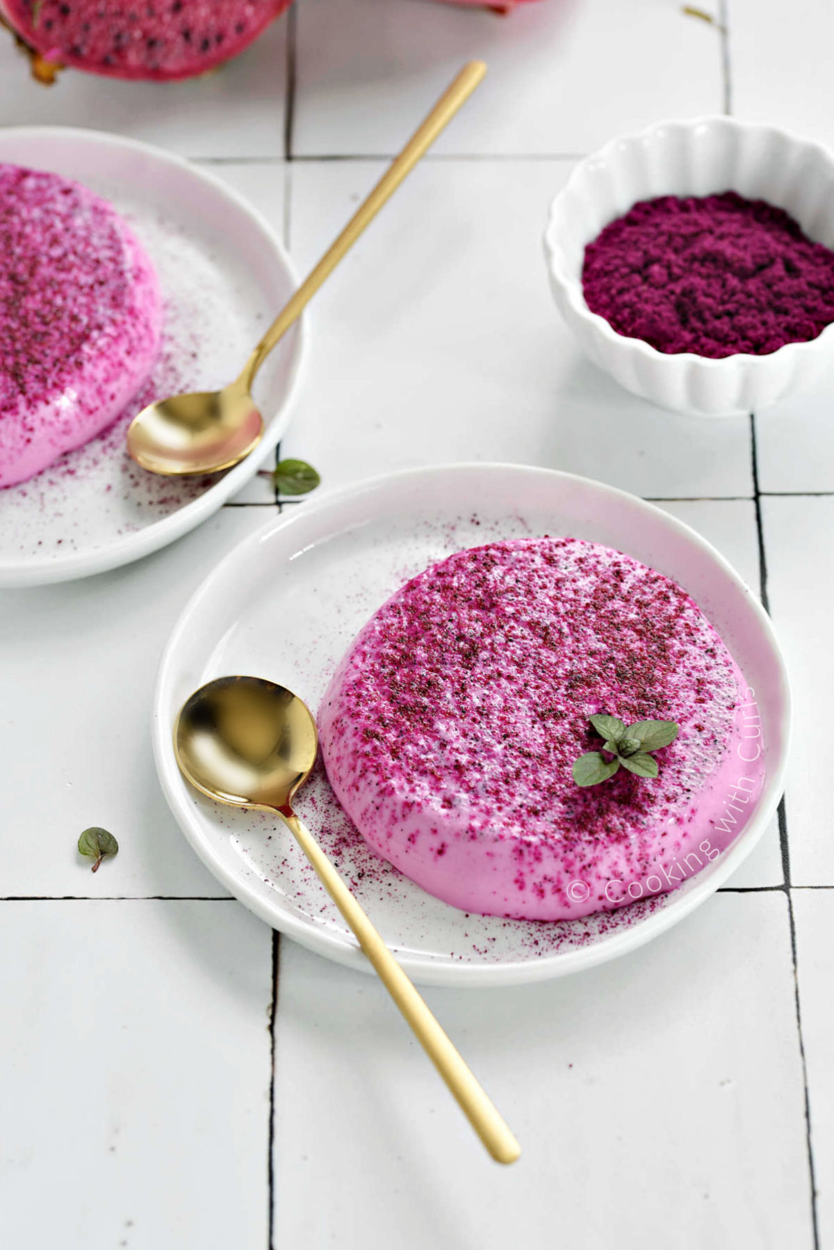 Two small plates with pink panna cotta sprinkled with dragon fruit powder.